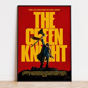 May include: A movie poster for The Green Knight featuring a figure standing on a dark rocky outcrop against a vibrant red background. The figure holds an axe aloft. Large yellow text reads THE GREEN KNIGHT, with additional credits and July 30 at the bottom.