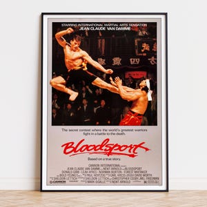 May include: A framed movie poster for Bloodsport featuring Jean-Claude Van Damme in a mid-air martial arts kick against an opponent. The poster includes the title in red text, the tagline The secret contest where the world's greatest warriors fight in a battle to the death, and full production credits.