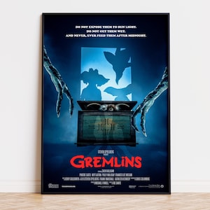 May include: A framed movie poster for Gremlins with a dark blue background. It features a wooden box with a creature inside, two clawed hands reaching from the sides, and the text: DO NOT EXPOSE THEM TO SUN LIGHT. DO NOT GET THEM WET. AND NEVER, EVER FEED THEM AFTER MIDNIGHT.