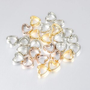 May include: A collection of open heart-shaped charms in assorted metallic finishes, including silver, gold, and rose gold tones. Each charm features a smooth, rounded frame with a hollow center, designed for use as jewelry components or craft accents.