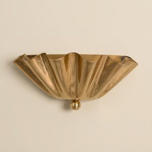 May include: A semi-circular wall sconce made of polished brass with a wide, ruffled, fan-like shade. The fixture features a smooth, curved metal surface with deep vertical pleats and a small, spherical brass knob at the bottom center point.