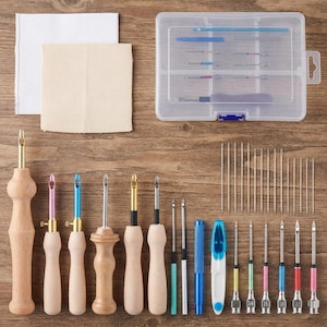 May include: A punch needle embroidery kit featuring a clear plastic storage case, two fabric squares, and an assortment of tools. Included are several wooden-handled punch needles, various metal needle tips, a seam ripper, and sewing needles.