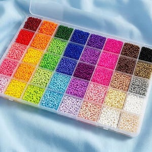 May include: A clear plastic storage container with a hinged lid, organized into forty-two individual square compartments. Each compartment is filled with small, round glass seed beads in a wide spectrum of solid colors, including red, orange, yellow, green, blue, purple, pink, brown, black, white, and various pastel shades.