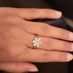 May include: A silver ring with a snowflake design. The ring is on a person's finger.