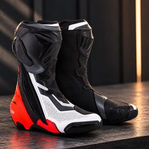 Puede incluir: Un par de botas de carreras para motocicleta con diseño de caña alta en colores negro, blanco y naranja brillante. Las botas incluyen protección reforzada en el tobillo, paneles de cuero blanco perforado, secciones de malla y un talón moldeado.