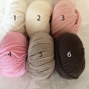 May include: Six skeins of yarn in various colors. The colors include white, cream, light pink, medium pink, tan, and dark brown. The yarn is tightly wound and ready for knitting or crocheting projects.