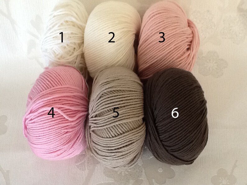 May include: Six skeins of yarn in various colors. The colors include white, cream, light pink, medium pink, tan, and dark brown. The yarn is tightly wound and ready for knitting or crocheting projects.