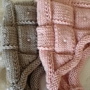 May include: Close-up of three knitted items in white, gray, and pink. The items have a woven design with small, clear beads. The texture of the knitwear is visible, highlighting the craftsmanship. The items appear to be soft and cozy.