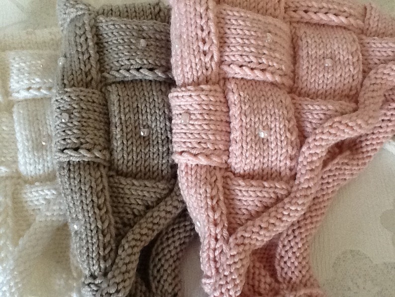 May include: Close-up of three knitted items in white, gray, and pink. The items have a woven design with small, clear beads. The texture of the knitwear is visible, highlighting the craftsmanship. The items appear to be soft and cozy.