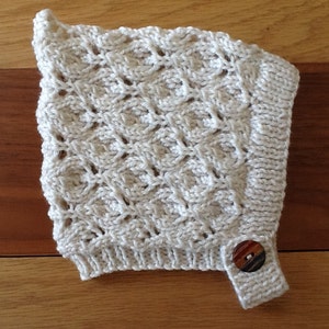 May include: A white crocheted baby bonnet with a button on the side.