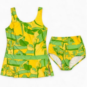 May include: A two-piece swimsuit set featuring a tank-style top with a skirted hem and matching high-waisted bottoms. The set is decorated with a vibrant yellow and green abstract floral pattern throughout, with a solid green horizontal band.