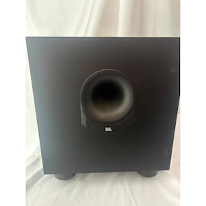 Peut inclure: Un caisson de basses JBL noir doté d'un boîtier carré avec un grand évent circulaire orienté vers l'avant. Le logo JBL est imprimé en blanc au bas du contour de l'évent. L'appareil repose sur quatre petits pieds arrondis.