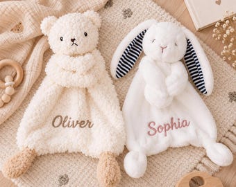 Puede incluir: Una manta de seguridad de peluche con forma de oso color crema bordada con el nombre Oliver y una manta de seguridad de peluche con forma de conejo blanco con orejas a rayas azul marino y blancas bordada con el nombre Sophia.