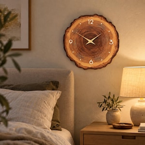 May include: A round wall clock made from a natural wood slice with visible tree rings. The clock face features gold-colored hands and white numerals at the 12, 3, 6, and 9 o'clock positions, with small white dots marking the remaining hours.
