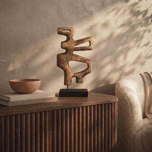 May include: A brown wooden abstract sculpture with organic, cutout shapes mounted on a thin metal rod and a rectangular black base. The sculpture features a smooth, polished grain texture and stands upright as a decorative tabletop object.