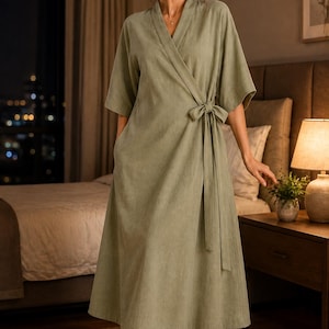 May include: A sage green wrap-style robe featuring a V-neckline, wide three-quarter length sleeves, and a matching fabric tie at the waist. The garment is floor-length with a straight hemline and includes side pockets, crafted from a solid-colored fabric.
