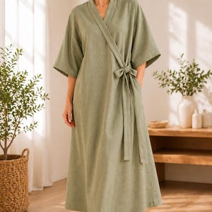 May include: A sage green wrap-style robe featuring a V-neckline, wide three-quarter length sleeves, and a matching fabric tie belt at the waist. The garment is floor-length with a clean, simple silhouette and a soft, textured fabric finish.