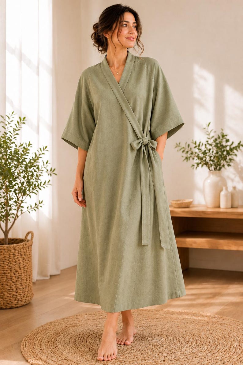 May include: A sage green wrap-style robe featuring a V-neckline, wide three-quarter length sleeves, and a matching fabric tie belt at the waist. The garment is floor-length with a clean, simple silhouette and a soft, textured fabric finish.