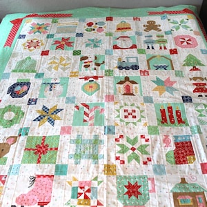 May include: A patchwork quilt featuring a grid of holiday-themed squares including a gingerbread person, Santa Claus, a train, a Christmas tree, a reindeer, candy canes, stockings, and various star patterns in red, green, white, and blue fabrics.
