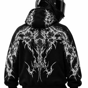 May include: A black hooded sweatshirt featuring a white, intricate, jagged, and symmetrical graphic print across the back and hood. The design resembles sharp, branching lightning or organic, thorny patterns that extend from the shoulders down.