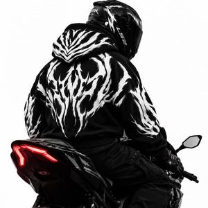 May include: A black hooded sweatshirt featuring a white tribal-inspired graphic print across the back and sleeves. The hoodie is worn by a rider in a black helmet sitting on a motorcycle with a visible red taillight against a white background.