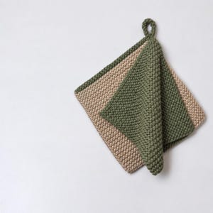 Peut inclure: Un manique carré crocheté à la main avec un motif de points dense et texturé. L'article est bicolore, composé d'une couche de base beige et d'une couche supérieure vert olive repliée, avec une petite boucle de suspension vert olive assortie.