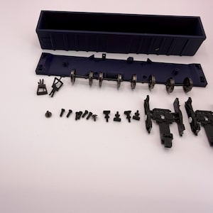 May include: A disassembled dark blue model train freight car kit including a rectangular cargo container, a flat undercarriage, metal wheel sets, two black truck assemblies, and various small plastic fasteners and coupling components.