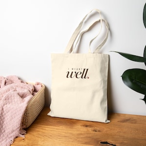Peut inclure: Un sac fourre-tout en toile de couleur crème avec deux bandoulières, présentant le texte brun foncé "I MEANT well." imprimé sur le devant, avec un petit point brun après le mot well.