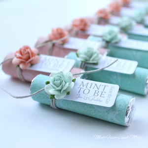 May include: Mint to be wedding favour boxes wrapped in turquoise and pink patterned paper with a small white flower and a tag that says "Mint to be" with the date and names of the couple.