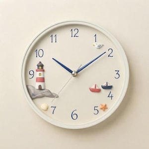 May include: A round wall clock with a cream-colored face and dark blue numerals. The clock features a 3D lighthouse on a gray rock, two small sailboats, a seagull, and a starfish. It has dark blue hour and minute hands and a thin silver second hand.