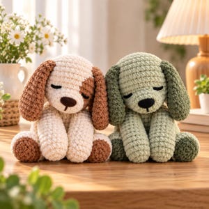Peut inclure: Deux jouets en peluche pour chiens faits à la main au crochet, assis côte à côte. Un chien est de couleur crème avec des oreilles marron et une tache marron sur un œil. L'autre est vert sauge avec des oreilles et des pattes vert foncé.