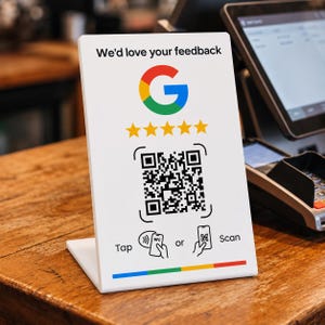 Könnte beinhalten: Ein weißes, rechteckiges Acrylschild mit dem Text We'd love your feedback, einem Google-Logo, fünf gelben Sternen, einem QR-Code sowie Symbolen für Tap or Scan. Am unteren Rand befindet sich ein horizontaler Balken mit blauen, roten, gelben und grünen Segmenten.