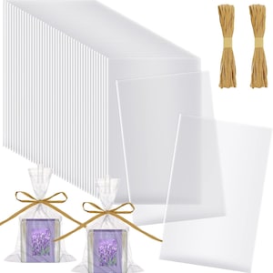 May include: A large collection of rectangular clear plastic display sheets arranged in a stack, accompanied by two bundles of tan raffia twine and two clear plastic gift bags containing small rectangular cards with lavender field imagery.