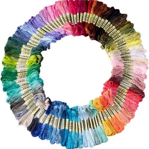 May include: A circular arrangement of numerous embroidery floss skeins in a wide spectrum of colors, including shades of blue, green, yellow, orange, red, pink, purple, brown, gray, and white, each featuring a small paper label with text.