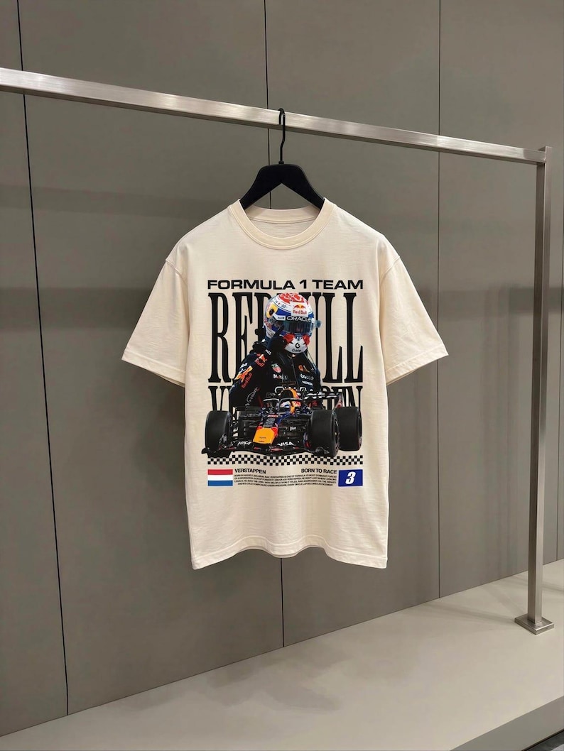 May include: A cream-colored short-sleeve t-shirt featuring a graphic print of a Formula 1 race car and driver. The text reads FORMULA 1 TEAM, RED BULL, VERSTAPPEN, BORN TO RACE, and the number 3, accompanied by a Dutch flag and checkered patterns.