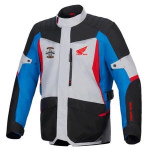 Puede incluir: Una chaqueta de moto con diseño de bloques de color gris claro, negro, azul y rojo. La chaqueta cuenta con cuello alto, un bolsillo vertical con cremallera en el pecho y el texto "FIRST RIDE" con un logotipo rojo en el pecho y la manga izquierda.