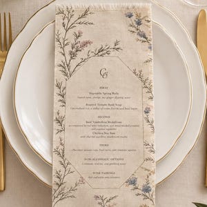 May include: A rectangular fabric menu with frayed edges, featuring a botanical print of small blue and pink flowers. The text lists courses including Vegetable Spring Rolls, Roasted Tomato Basil Soup, Beef Tenderloin Medallions, and Chicken Sea Bass.