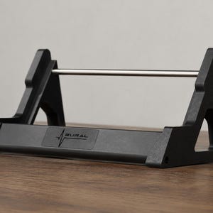 May include: A black matte display stand featuring two triangular side supports connected by a horizontal silver metal rod. The front base of the stand displays the text NEURAL with a stylized heartbeat line graphic integrated into the lettering.
