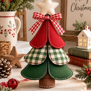 Puede incluir: Un adorno de árbol de Navidad de tela con tres niveles de paneles redondeados superpuestos en rojo sólido, verde y cuadros vichy blancos, rematado con una estrella color crema y un lazo de cuadros vichy rojo y blanco sobre una base cilíndrica marrón.