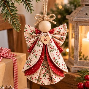 May include: A hanging angel ornament featuring a smooth wooden bead head, a jute twine loop, and a layered fabric dress. The dress combines cream fabric with a red and green floral print and solid red fabric, accented by a small wooden heart button.