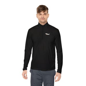 Può includere: Una maglia nera a maniche lunghe con zip a un quarto e un piccolo logo RM bianco e rosso sul petto sinistro. Il capo presenta un colletto alto con chiusura a zip centrale e maniche lunghe, abbinato a pantaloni grigio scuro.