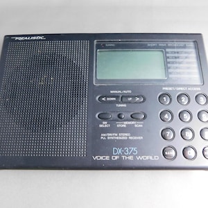 May include: Black Realistic DX-375 shortwave broadcast radio. It has a digital display, number pad, and function buttons. The text "VOICE OF THE WORLD" is printed on the front.