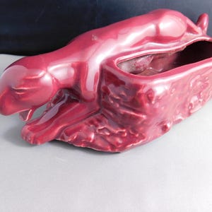 May include: A burgundy ceramic planter shaped like a panther lying down. The planter has a textured surface and a hollowed-out back for planting.