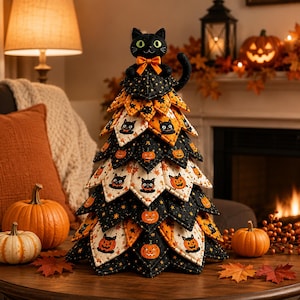 May include: A fabric tabletop tree decoration featuring layered, pointed leaves in black and white patterns with orange pumpkins and black cat illustrations. A plush black cat with a bright orange bow sits at the top of the conical structure.