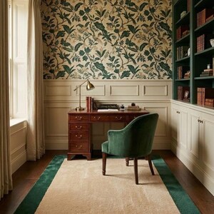 Puede incluir: Una oficina en casa con un escritorio de madera oscura con cajones, un sill&oacute;n de terciopelo verde y una alfombra rectangular con centro beige y borde verde. La habitaci&oacute;n incluye estanter&iacute;as verdes integradas, frisos color crema y papel tapiz floral.