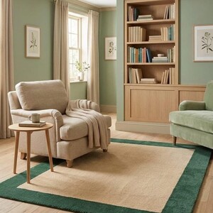 Puede incluir: Una alfombra rectangular que presenta un gran panel central de color beige enmarcado por un borde ancho de color verde oscuro. La alfombra se coloca sobre un suelo de madera clara en una habitaci&oacute;n con paredes verde salvia y una estanter&iacute;a.