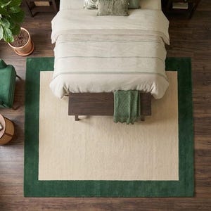 Puede incluir: Una alfombra rectangular que presenta un gran panel central de color crema enmarcado por un borde ancho de color verde oscuro s&oacute;lido. La alfombra est&aacute; colocada sobre un suelo de madera oscura bajo una cama con ropa de cama crema, un banco y cojines verdes.