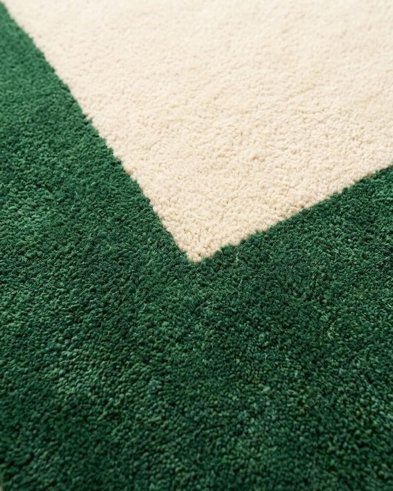 Puede incluir: Una alfombra de pelo largo con un dise&ntilde;o geom&eacute;trico que presenta un borde de color verde bosque profundo y una secci&oacute;n central en color crema. La textura es gruesa y afelpada, mostrando una clara transici&oacute;n diagonal entre los dos colores.