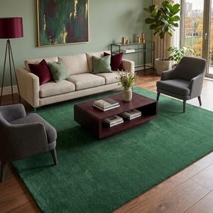 Könnte beinhalten: Ein Wohnzimmer mit einem großen rechteckigen grünen Teppich auf einem Holzboden, einem beigen Sofa mit weinroten und grünen Kissen, zwei grauen Sesseln, einem Couchtisch aus dunklem Holz, einer Stehlampe und einem gerahmten abstrakten Gemälde.