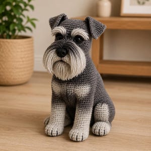 Puede incluir: Una figura de perro schnauzer tejida a mano en ganchillo con hilo gris oscuro en el cuerpo y la cabeza, con detalles en gris claro en las patas y el pecho. El perro tiene una barba y cejas texturizadas en gris claro y ojos de plástico negro.